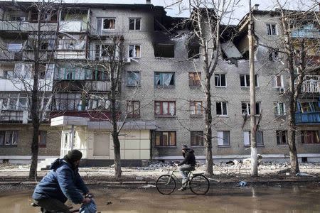 Men ride bicycles past a building which was damaged by fighting in the town of Debaltseve February 23, 2015. REUTERS/Baz Ratner