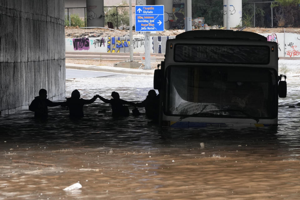 Passengers are silhouetted as they wade through high water after evacuating a bus stuck in a flooded underpass in southern Athens, Thursday, Oct. 14, 2021. Storms have been battering the Greek capital and other parts of southern Greece, causing traffic disruption and some road closures. (AP Photo/Thanassis Stavrakis)