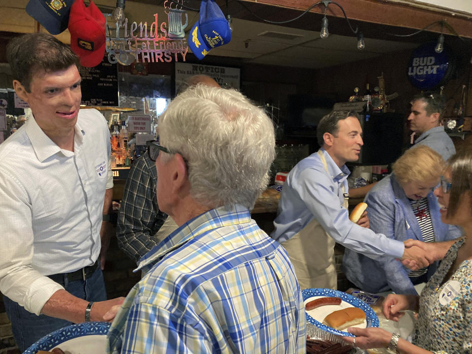 Retired Army Capt. Sam Brown, left, and Nevada Republican Senate candidate Adam Laxalt, in apron, right, greet veterans and their guests while serving up free hotdogs at the VFW post in Reno, Nev., on Sept. 1, 2022. Brown, who was nearly killed during combat in Afghanistan and lost the GOP Senate primary to Laxalt, is now rallying behind the campaign of Laxalt, who served as a Navy Judge Advocate General in Iraq and is trying to unseat Sen. Catherine Cortez Masto, D-Nev. (AP Photo/Scott Sonner)