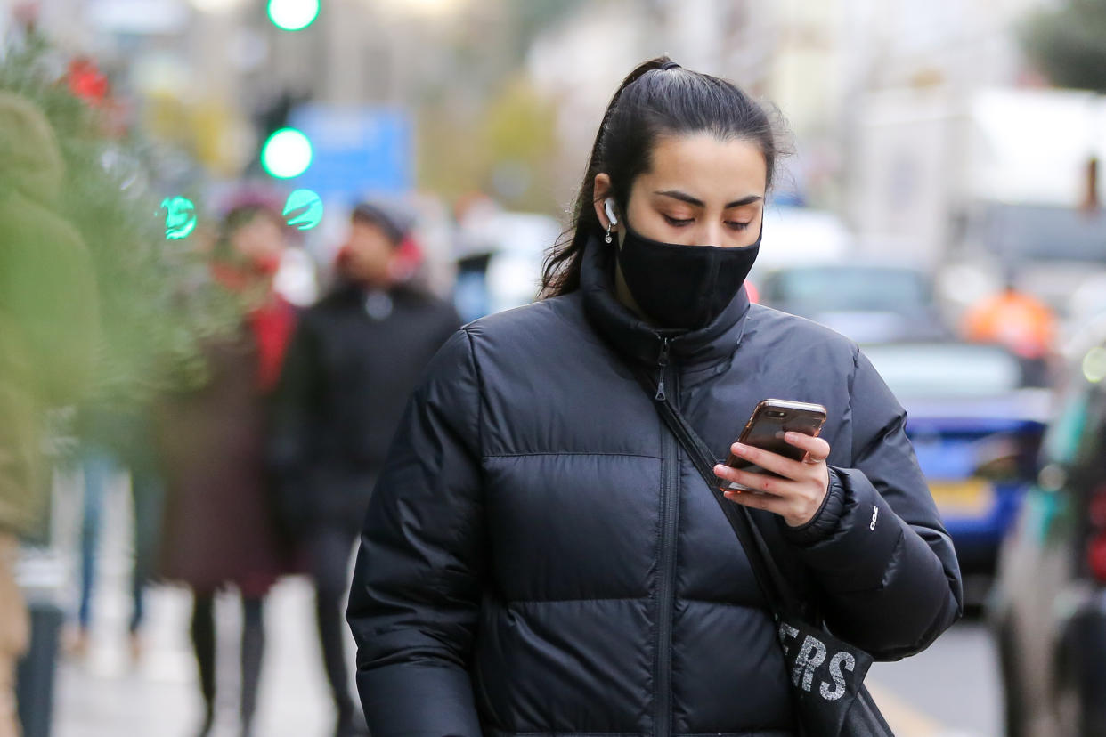 A woman wearing a face mask looks at her mobile phone while walking on the street. (Photo by Dinendra Haria / SOPA Images/Sipa USA)