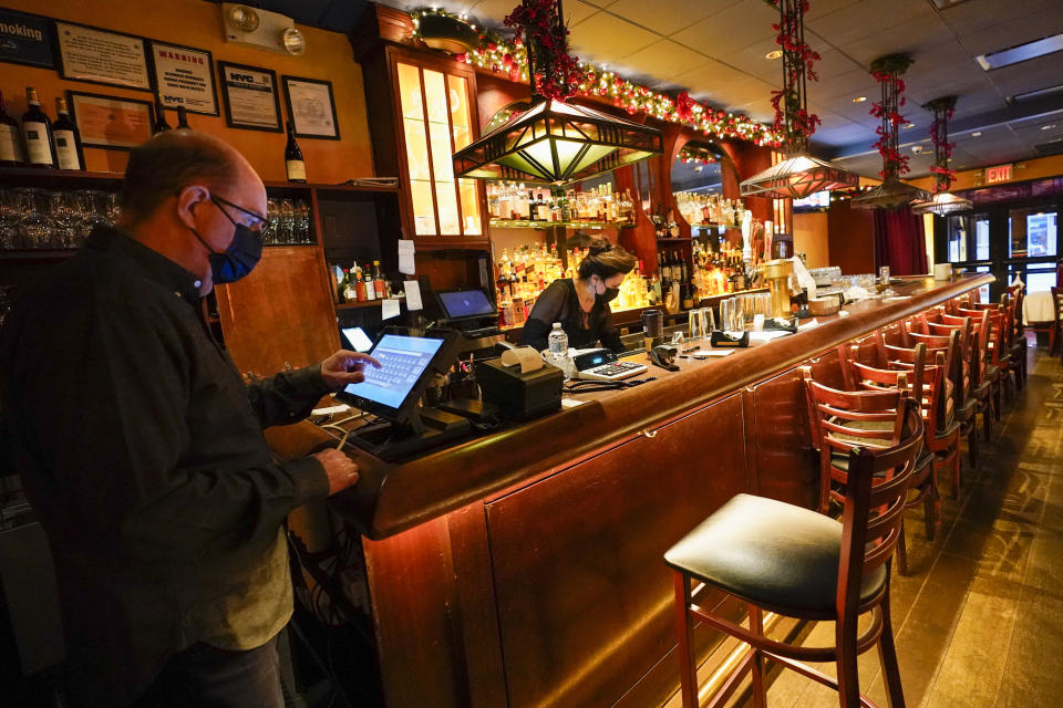 Steve Olsen, left, owner of the West Bank Café, sends a to-go order to the kitchen as Janet Momjian works at the bar in the empty restaurant, Saturday, Jan. 9, 2021, in the Hell's Kitchen neighborhood of New York. The boarded-up windows and For Rent signs are all over the place in Manhattan’s Hell’s Kitchen neighborhood. Nearby, the Broadway theaters are all dark. But the economic darkness brought on by the coronavirus pandemic has had a few bright spots. A couple of well-loved venues have gotten financial boosts, thanks to online fundraising campaigns and even a telethon. (AP Photo/Mary Altaffer)