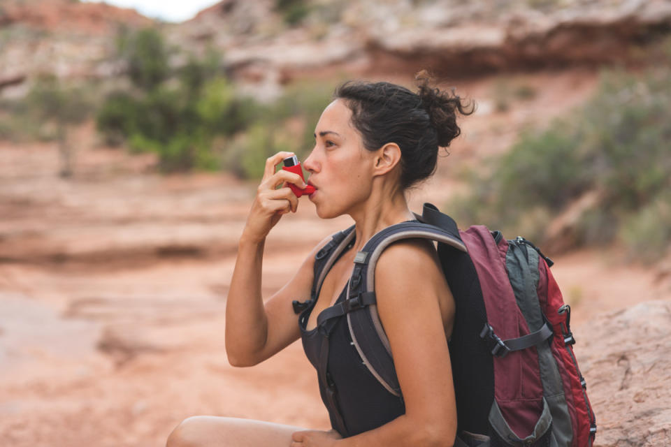 Woman using an inhaler while hiking.<p>iStock</p>