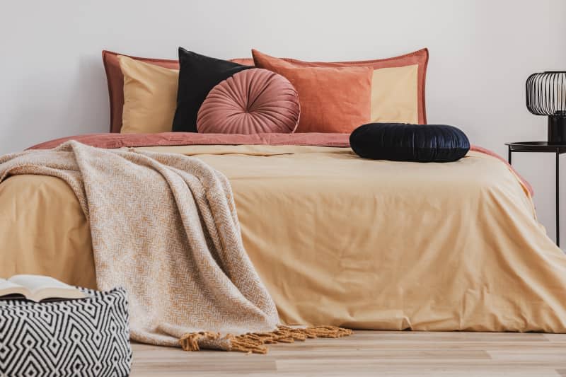 Open book on patterned pouf in colorful bedroom interior. pintuck round pillows on bed