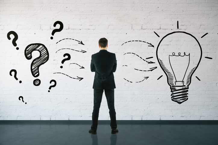 A man, seen from behind, looks at a wall showing drawings of question marks to his left, with arrows pointing to a light bulb on his right.
