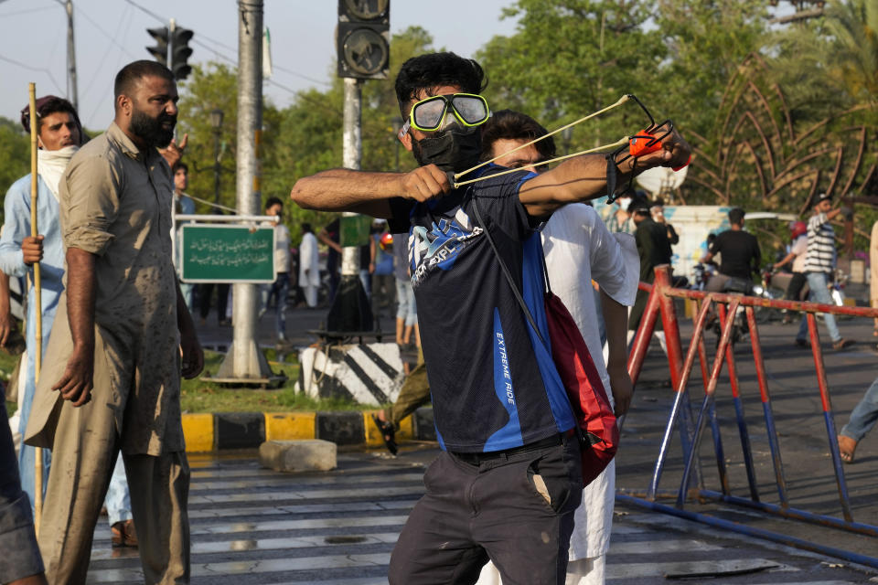 A supporter of Pakistan's former Prime Minister Imran Khan throws stones using a slingshot toward police officers during a protest against the arrest of their leader, in Lahore, Pakistan, Tuesday, May 9, 2023. Khan was arrested Tuesday as he appeared in a court in the country’s capital, Islamabad, to face charges in multiple graft cases. Security agents dragged Khan outside and shoved him into an armored car before whisking him away. (AP Photo/K.M. Chaudary)