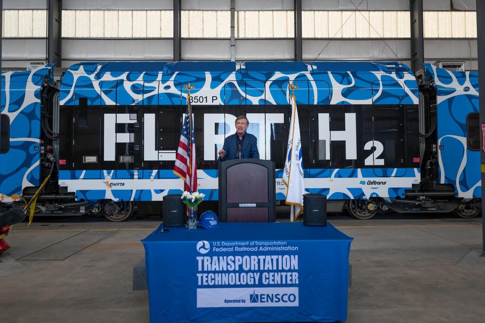 Sen. John Hickenlooper speaks with the Stadler FLIRT H2 hydrogen-powered train as a backdrop at the Transportation Technology Center on Thursday, April 4, 2024.