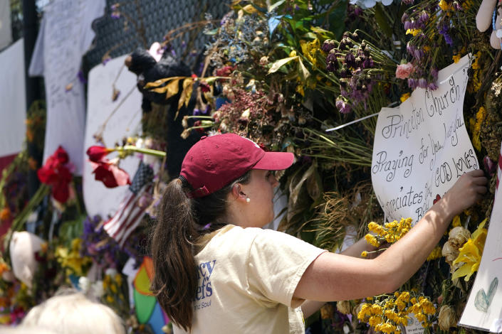 Molly MacDonald, with Mercy Chefs, hangs a sign on behalf of Princeton Church at a makeshift memorial remembering the victims of the nearby collapsed Champlain Towers South building, Wednesday, July 14, 2021, in Surfside, Fla. Mercy Chefs has set up a mobile kitchen to feed search and rescue teams working at the site three meals a day. (AP Photo/Lynne Sladky)