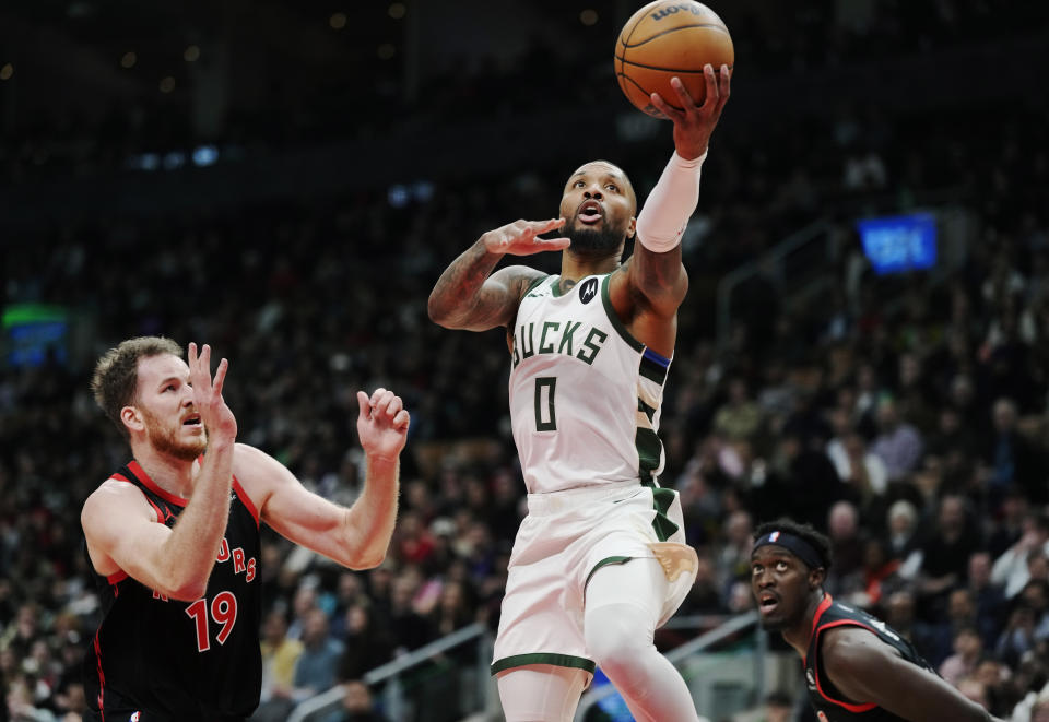 Milwaukee Bucks' Damian Lillard (0) drives between Toronto Raptors' Jakob Poeltl (19) and Pascal Siakam during the first half of an NBA basketball game Wednesday, Nov. 15, 2023, in Toronto. (Frank Gunn/The Canadian Press via AP)