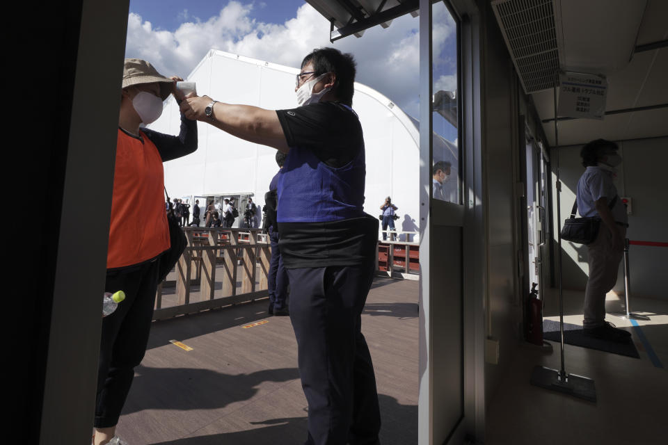 A staff member checks a body temperature in a screening test for spectators and officials to ensure a safe and secure Toyo Olympic Games Wednesday, Oct. 21, 2020, in Tokyo. Tokyo Olympic officials say they don't know exactly what measures will be taken against the COVID-19 pandemic at next year's Games, but they want the world to know they're working on it. (AP Photo/Eugene Hoshiko)