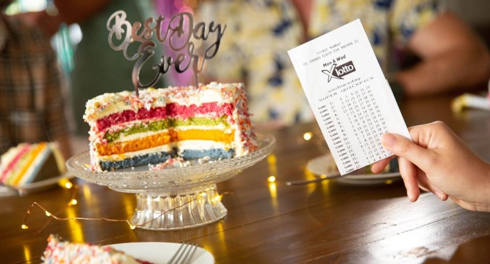 Person holds winning lotto ticket in front of best day ever cake