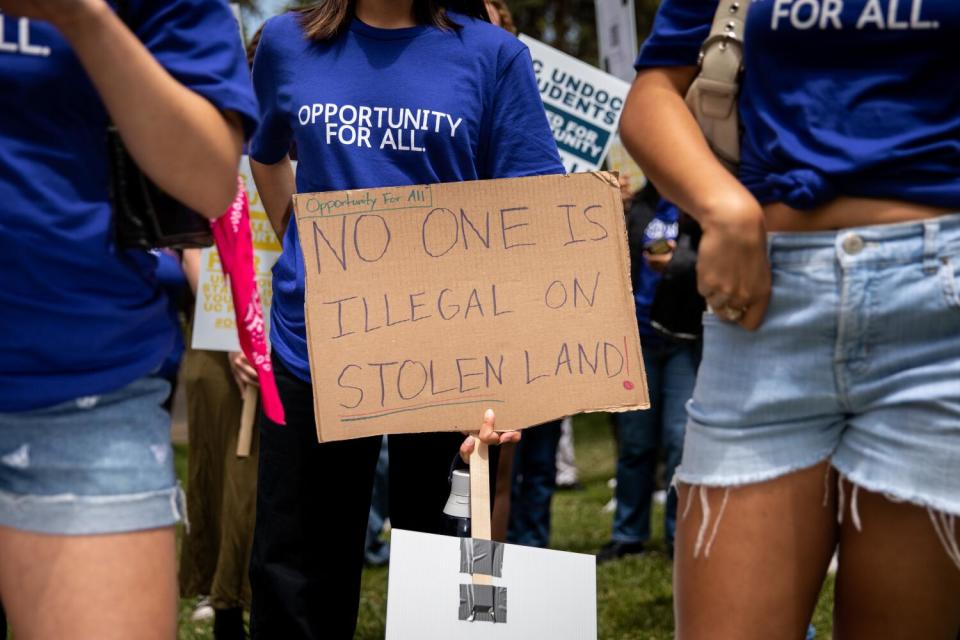 A group of demonstrators, one holding a sign that reads, "No one is illegal on stolen land!"