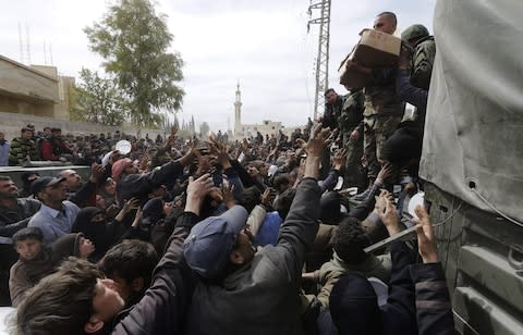 Syrian civilians evacuated from the Eastern Ghouta enclave reach out to receive food distributed by Syrian soldiers as they pass the regime-controlled corridor opened by the government forces - Credit: AFP