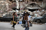 Women walk past destroyed cars at a neighborhood near the scene of Tuesday's explosion that hit the seaport of Beirut, Lebanon, Friday, Aug. 7, 2020. Rescue teams were still searching the rubble of Beirut's port for bodies on Friday, nearly three days after a massive explosion sent a wave of destruction through Lebanon's capital. (AP Photo/Thibault Camus)