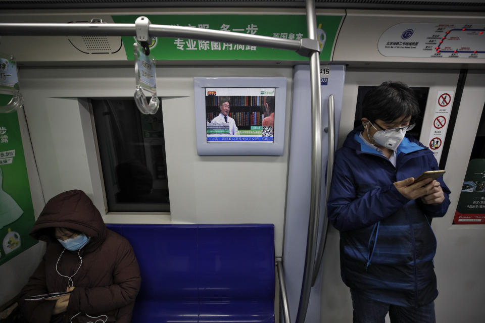 Pasajeros con mascarilla en un tren del metro, mientras una pantalla muestra a un médico hablando sobre precauciones contra un nuevo coronavirus, en Beijing, el lunes 17 de febrero de 2020. (AP Foto/Andy Wong)