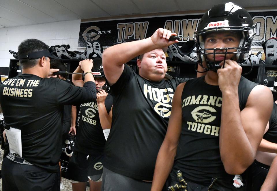 Joe Bogle, one of the Comanche football coaches, adjusts the helmet of a player.