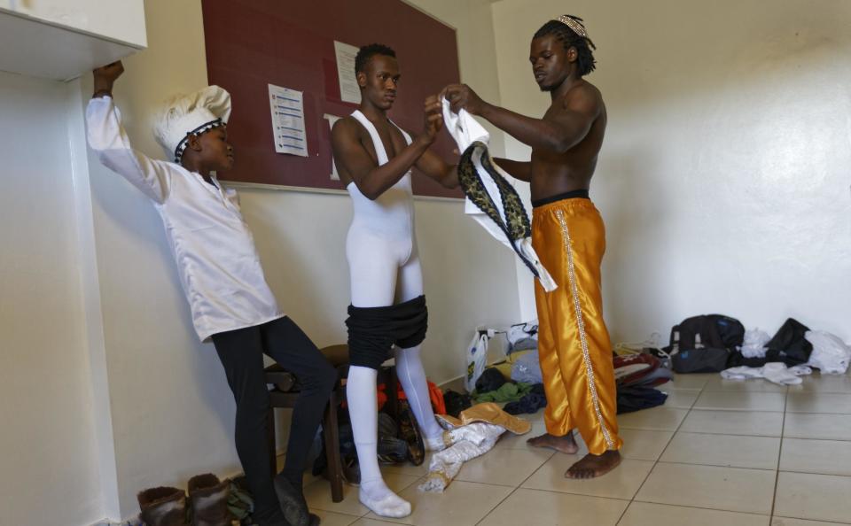 In this photo taken Friday, Dec. 9, 2016, Kenyan ballet dancer Joel Kioko, 16, center, is helped to put on his costume by dance teacher Victor Mishael Okumu, right, before a performance of The Nutcracker in Nairobi, Kenya. In a country not usually associated with classical ballet, Kenya's most promising young ballet dancer Joel Kioko has come home for Christmas from his training in the United States, to dance a solo in The Nutcracker and teach holiday classes to aspiring dancers in Kibera, the Kenyan capital's largest slum. (AP Photo/Ben Curtis)