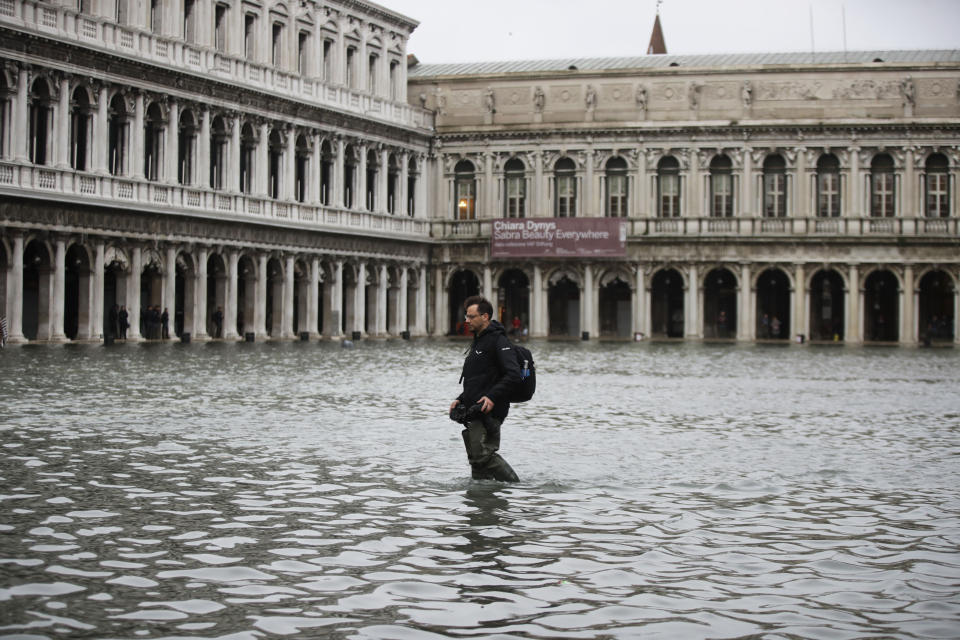 A man holds his cameras as he walks in a flooded St. Mark's Square in Venice, Italy, Friday, Nov. 15, 2019. The high-water mark hit 187 centimeters (74 inches) late Tuesday, Nov. 12, 2019, meaning more than 85% of the city was flooded. The highest level ever recorded was 194 centimeters (76 inches) during infamous flooding in 1966. (AP Photo/Luca Bruno)