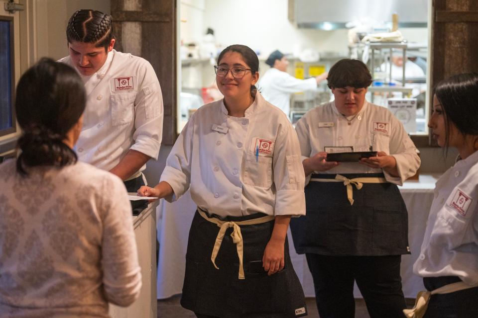 Student servers listen to Laura Nicola, a dining room instructor, before dinner service.