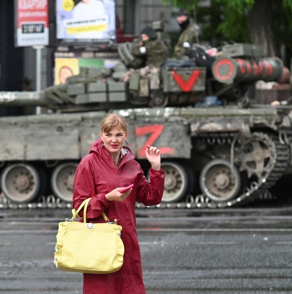 A woman walks past fighters of Wagner private mercenary group in a street near the headquarters of the Southern Military District in the city of Rostov-on-Don