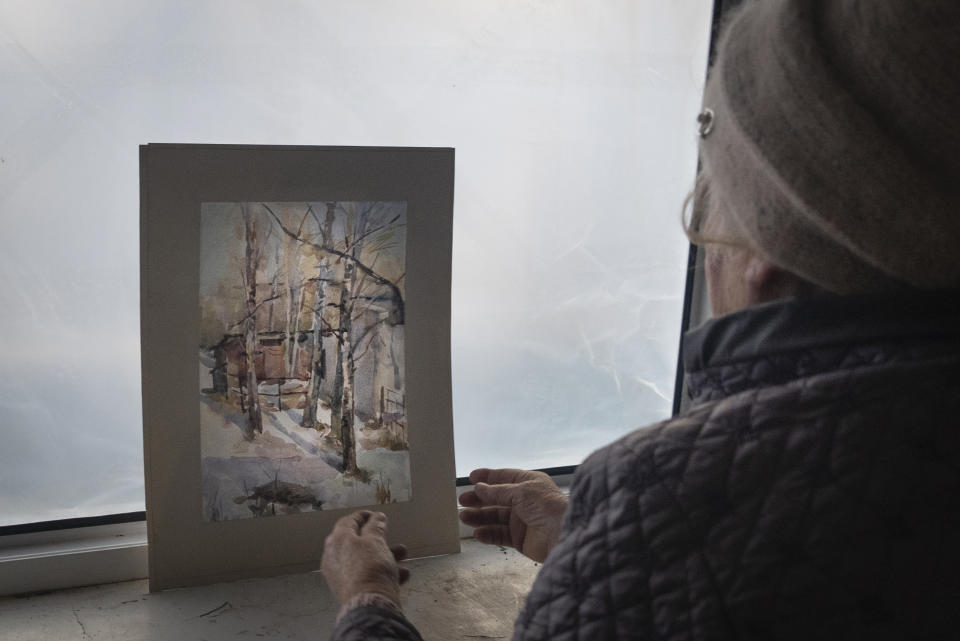 Liudmyla, 78, Mykola's Soloviov wife, holds up her husband's painting of the landscapes seen from the window in the room of their apartment damaged by a missile attack in Sloviansk, a city in Donetsk region, his hometown which lies 25 kilometers from the frontline, Ukraine, Saturday, Jan. 27, 2024. Soloviov, 88, is a painter the world does not know. His expressive and imaginative landscapes of eastern Ukraine encapsulate a lost time, and lie undiscovered, tucked away in a modest home under threat of Russian attack. (AP Photo/Vasilisa Stepanenko)