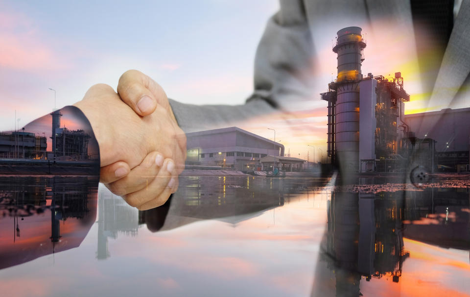 Two people shaking hands near an energy facility.