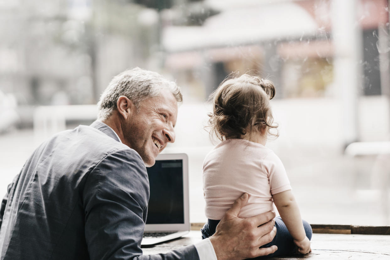 Businessman with little daughter working on laptop in cafe