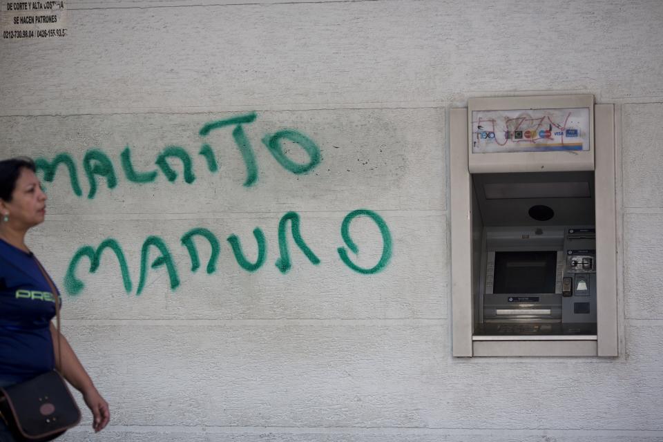 FILE - In this Aug. 20, 2018 file photo, a wall is spray painted with a message that reads in Spanish, "Damn Maduro" next to an ATM machine in Caracas, Venezuela. A new currency with six fewer zeros debuts Friday, Oct. 1, 2021, in Venezuela, whose currency has been made nearly worthless by years of the world's worst inflation. (AP Photo/Ariana Cubillos, File)