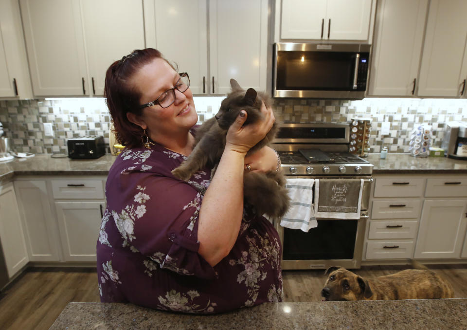 Victoria Sinclaire holds her cat Toby, that survived the Camp Fire, as her dog Joey looks on at her recently rebuilt home in Paradise, Calif., Tuesday, Nov. 5, 2019. Unable to get Toby and another of her pet cats, it took Sinclaire six hours to escape the flames from last year's wildfire that destroyed 90 percent of Paradise. (AP Photo/Rich Pedroncelli)