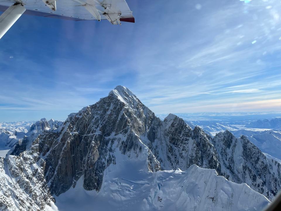 A view of a mountain peak with snow outside of a plane window