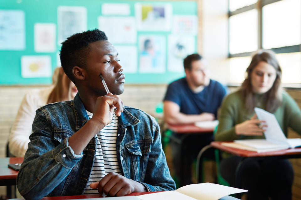 Students sitting in a classroom, with the focus on one thoughtful-looking young man