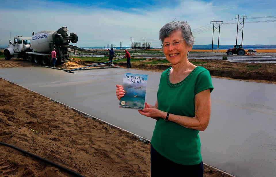 Author Helen Lingscheit Heavirland holds her book, Surviving the Sand: My Family’s Struggle to Farm the Pasco Desert, on the Franklin County farmland she moved to with her family as a seven-year-old in 1954. Heavirland is having a concrete slab poured on the farm for a manufactured home so she can soon move from Walla Walla back to where she grew up.