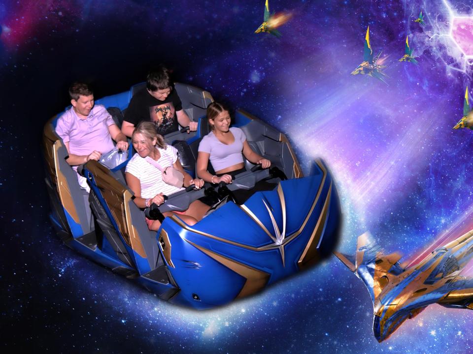 Image of Terri Peters and her two kids and husband on a roller coaster ride. Terri looks to the right laughing and her family looks down. The photo is edited to make it look like they're flying through a galaxy with spaceships flying at them.