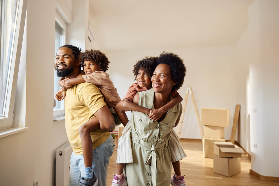 Happy black parents having fun while piggybacking their small kids after relocating into new apartment.