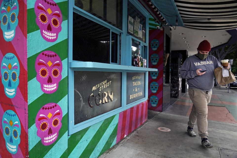 A person picks up food to go at "Tacos Tu Madre," restaurant in Los Angeles Monday, Jan. 25, 2021. California has lifted regional stay-at-home orders statewide in response to improving coronavirus conditions. Public health officials said Monday that the state will return to a system of county-by-county restrictions intended to stem the spread of the virus. Local officials could choose to continue stricter rules. The state is also lifting a 10 p.m. to 5 a.m. curfew. (AP Photo/Damian Dovarganes)