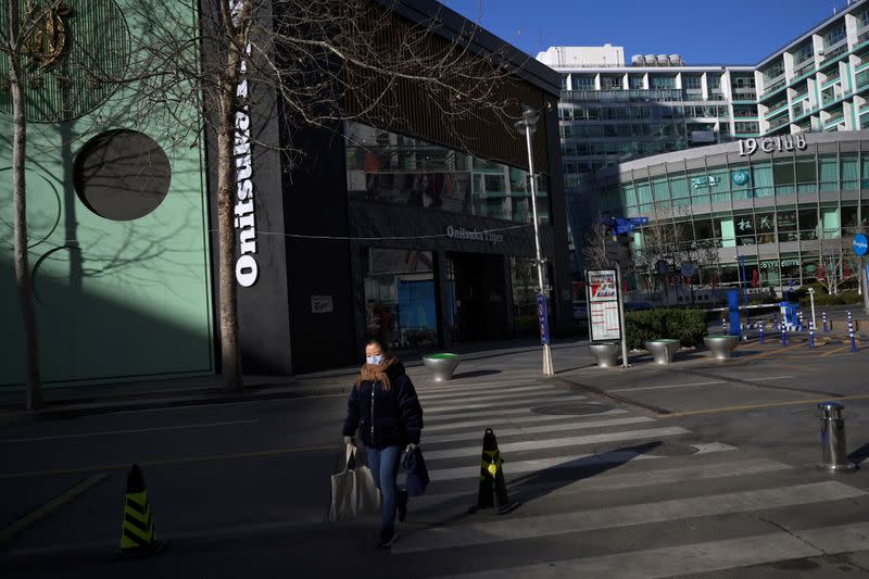 Woman wearing a face mask walks across a street at a shopping area, in Beijing's central business district