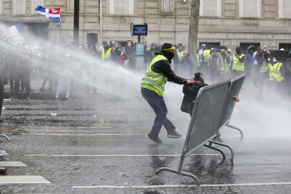 A yellow vests demonstrator rescues another one as police forces use water cannons, Saturday, March 16, 2019 in Paris. French yellow vest protesters clashed Saturday with riot police near the Arc de Triomphe as they kicked off their 18th straight weekend of demonstrations against President Emmanuel Macron. (AP Photo/Christophe Ena)