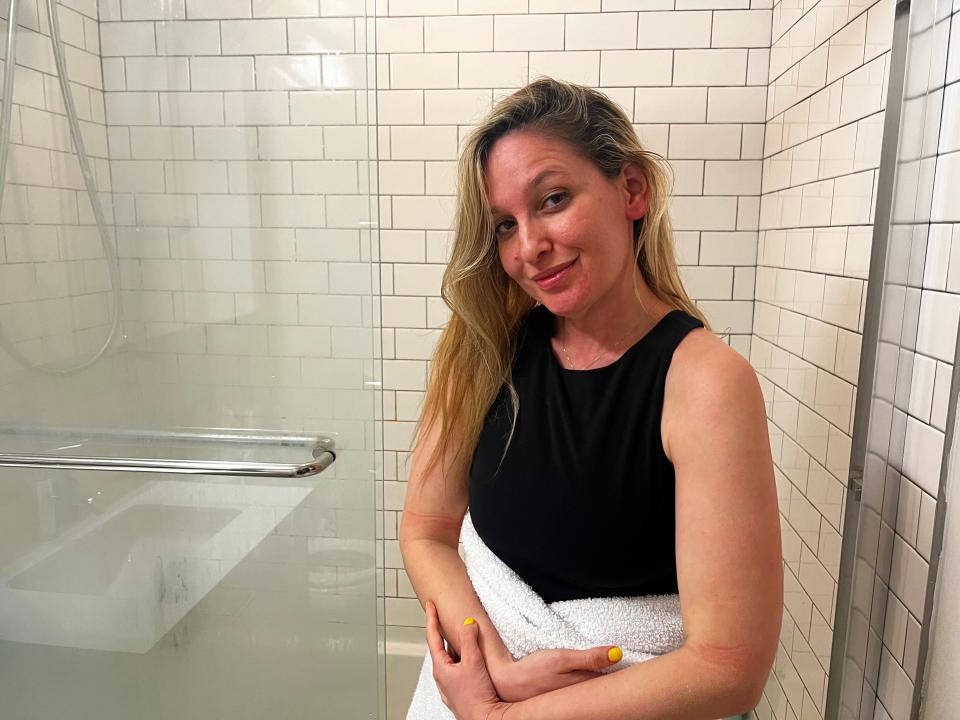 jen standing in front of her shower wearing clothes and wrapped in a towel