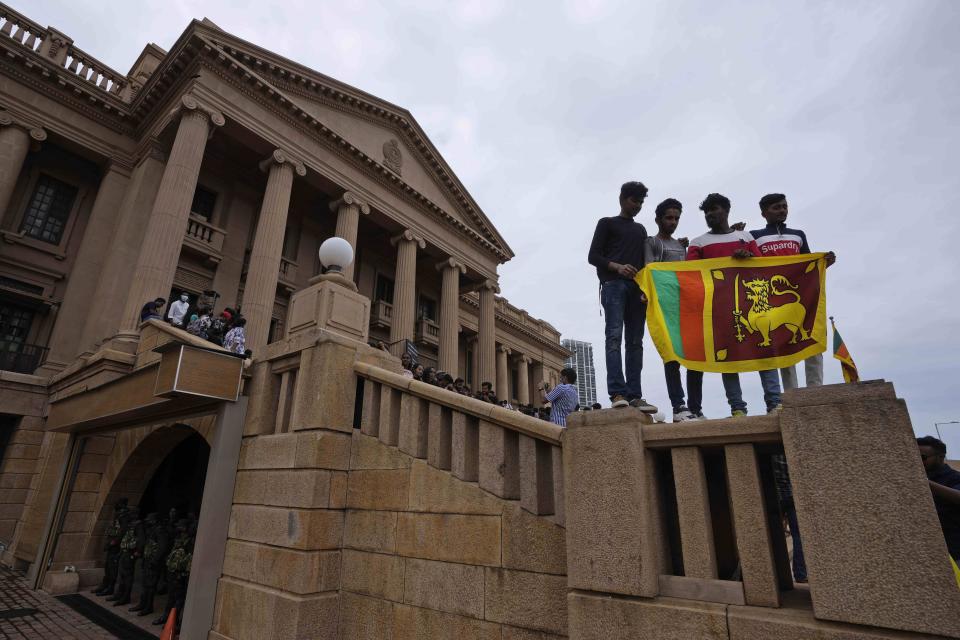 People stand holding a national flag at the President Gotabaya Rajapaksa's office on the second day after it was stormed in Colombo, Sri Lanka, Monday, July 11, 2022. Sri Lanka is in a political vacuum for a second day Monday with opposition leaders yet to agree on who should replace its roundly rejected leaders, whose residences are occupied by protesters, angry over the country's economic woes. (AP Photo/Eranga Jayawardena)