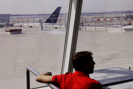 A man sits at a table in front of the tail of a Saudia Airlines plane stands at a gate at JFK International Airport in New York, U.S., March 21, 2017. REUTERS/Lucas Jackson