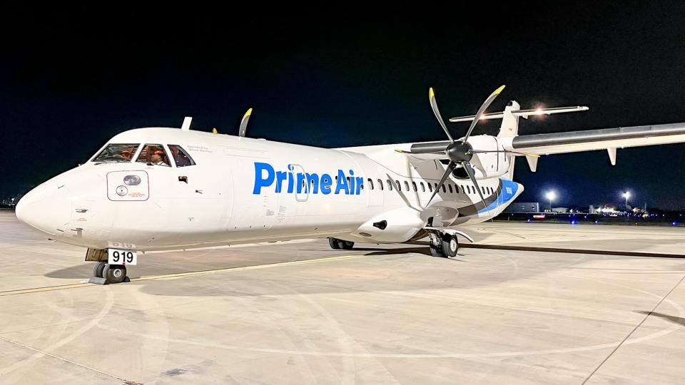 A small propeller plane in the Amazon Prime Air logo on the tarmac at night.