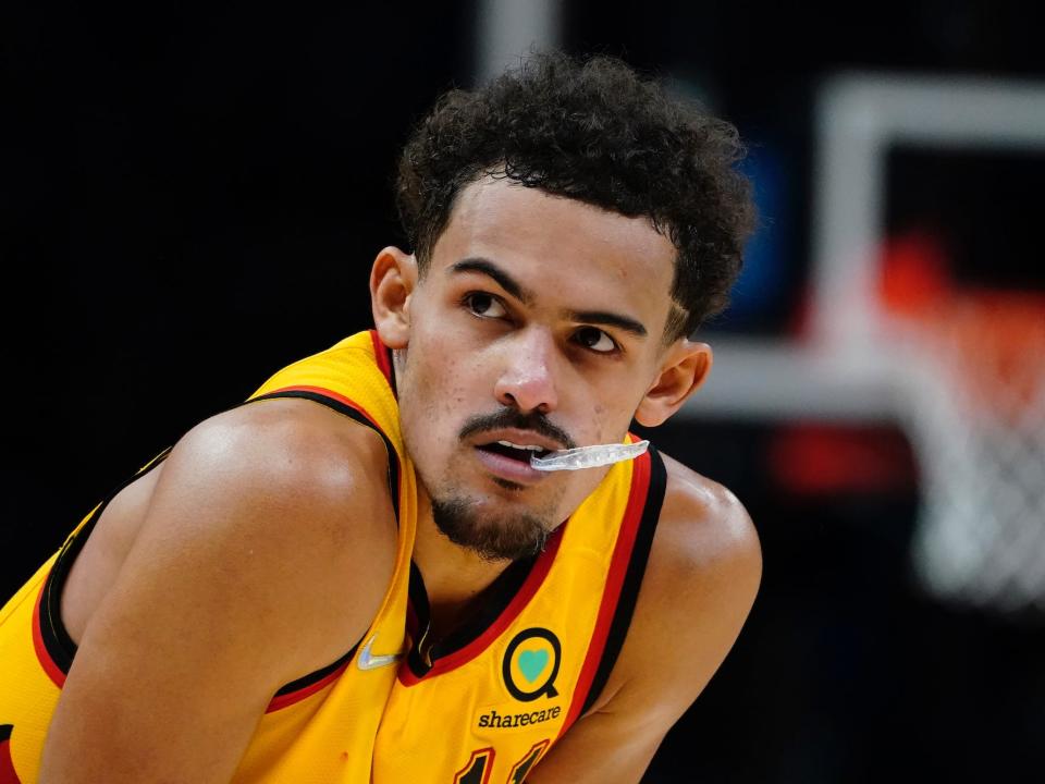 Trae Young bites on his mouthguard while standing with his hands on his knees.