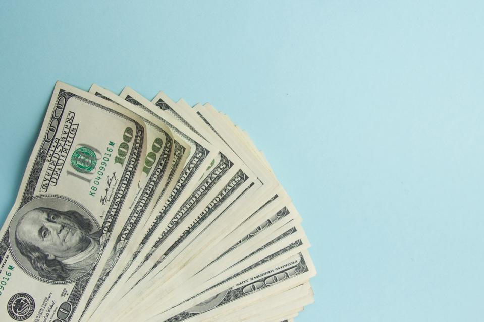 Stack of U.S. hundred dollar bills fanned out over a blue background.