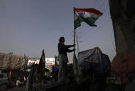 An Indian farmer erects the Indian flag after arriving at the Delhi-Uttar Pradesh border for Tuesday's tractor rally in New Delhi, India, Monday, Jan. 25, 2021. Thousands of farmers gathered on the borders of Delhi for a massive tractor rally on Tuesday against the three contentious farm laws when India will celebrate its Republic day with a military and cultural parade. The two-month-old old blockade of highways connecting the capital with the country's north continues as the talks have remained deadlocked with the government refusing to scrap the new agricultural reform laws which the farmers say will benefit large corporations. (AP Photo/Manish Swarup)