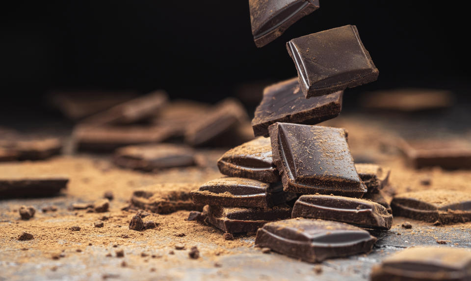 Falling broken chocolate bars on black slate background with cocoa powder, stack of dark chocolate pieces