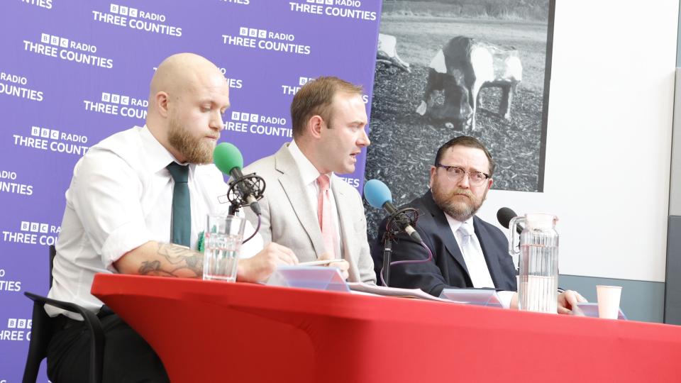 Three of the candidates in the Mid Bedfordshire debate sitting at a table speaking into microphones