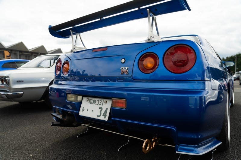a close-up shot of the rear of an R34 nissan gt-r in blue, with a high wing on the trunk lid