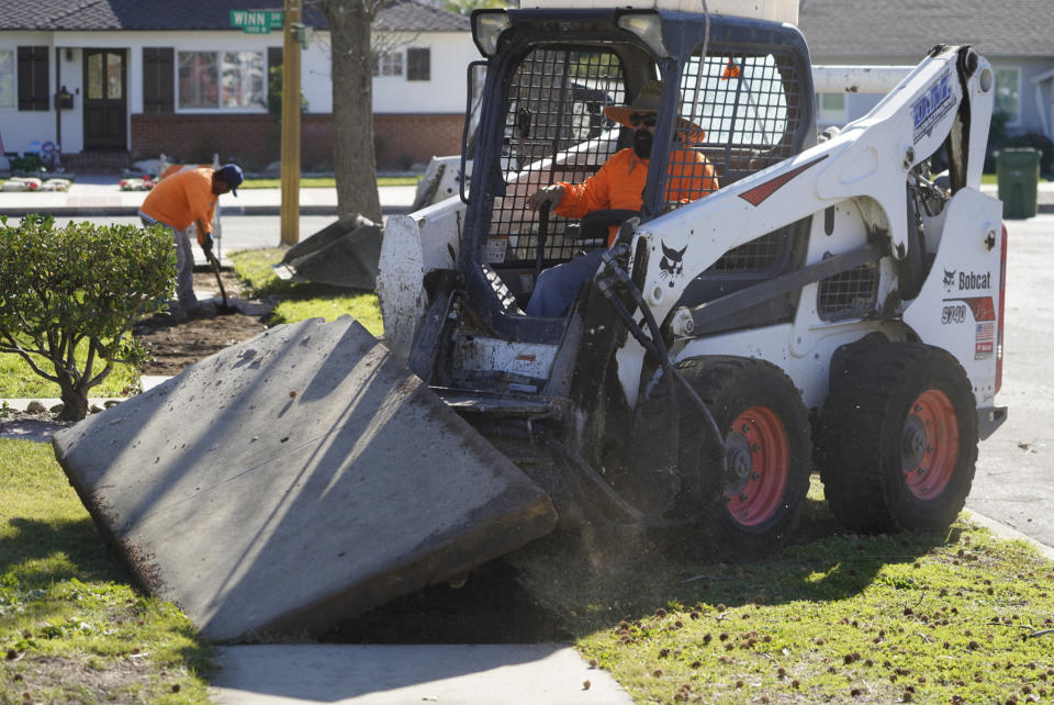 Contractor Robert Martinez removes broken concrete blocks from a sidewalk in Upland, Calif., on Monday, Jan. 24, 2022. After estimating a loss in revenue in the early months of the pandemic in 2020, city officials say Upland is now doing well financially, boosted partly by federal pandemic aid. The city plans to use part of that aid to repave parking lots and repair hundreds of sections of sidewalks. (AP Photo/Damian Dovarganes)