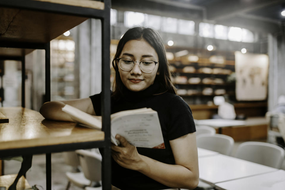 A girl leaning against a shelf reading