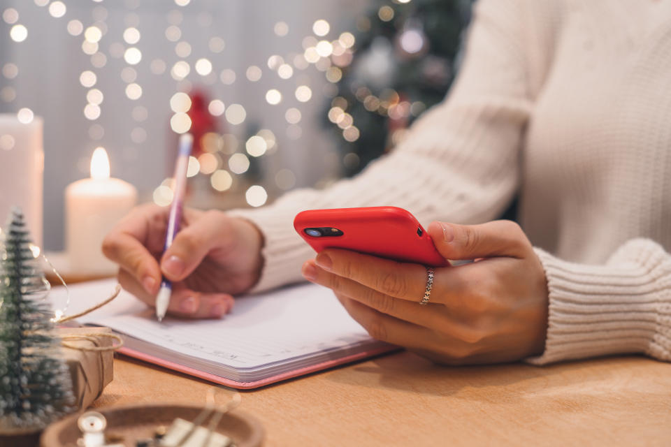 Goals plans make to do and wish list for new year christmas concept writing in notebook. Woman hand holding pen on notepad and cellphone at home on winter holidays xmas.