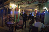 Police officers talk with the owner of a bar as people sit at the terrace in Fuengirola, near Malaga, Spain, Saturday, Aug. 8, 2020. The increase in Spain of coronavirus outbreaks associated with nightlife has set off alarms in recent days, mainly in tourist areas where pubs and discos are full before the summer tourist campaign. (AP Photo/Jesus Merida)